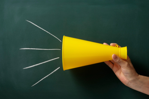 Yellow megaphone with hand  in front of  blackboard.