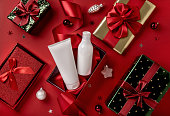 White bottles cosmetic products in red giftbox and on red background. Christmas sale of beauty products concept. Top view with place for text.
