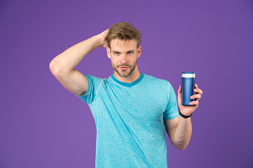 Handsome man with sexy body isolated on purple background. Model with perfect hair holding shampoo bottle, bodycare and costetics concept.