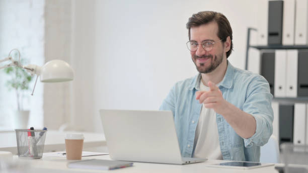 istock Young Man with Laptop Pointing at Camera 1347075805