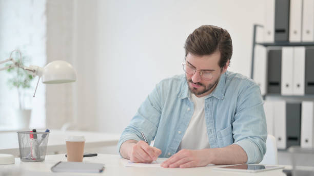 istock Young Man Writing on Paper in Office 1347077353
