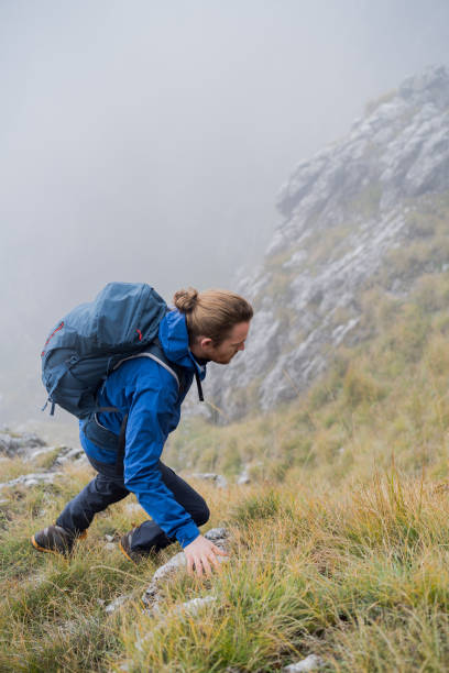 istock Man hikes up grassy mountain ridge through fog 1347078968