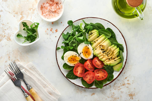 istock Avocado, cherry tomato, spinach and chicken egg, microgreens peas and black sesame seeds fresh salad in bowl on white stone table background. Healthy breakfast food concept. Top view. 1347083136
