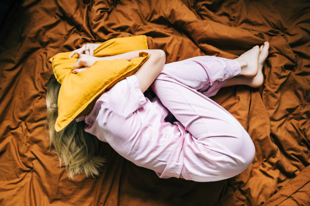 Depressed caucasian millennial woman lying alone on bed and covering head with pillow feeling afraid, top view. stock photo