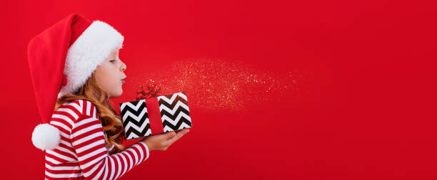 weihnachtsbannerkind mit weihnachtsmannmütze, das ein geschenk auf rotem hintergrund mit platz für text hält - 1 2 months stock-fotos und bilder