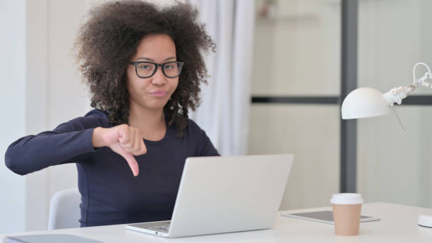 daumen runter von afrikanerin mit laptop - disappointment hand sign gesturing young adult stock-fotos und bilder