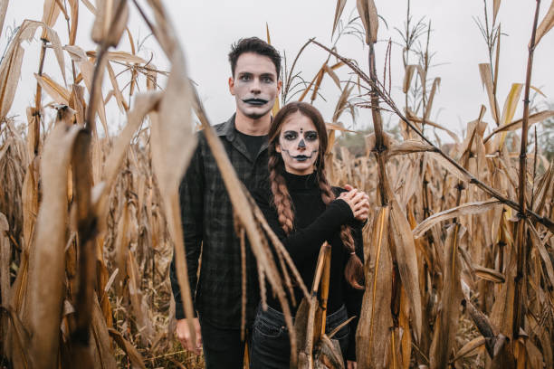 Spooky young couple in Halloween costumes in a cornfield standing one in front of the other and holding hands