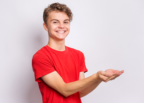 Smiling teen boy holding nothing. Happy teenager with empty palms up, over grey background. Child stretched out his hands - sign of begging or giving.