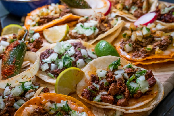 assortment of delicious authentic tacos, birria, carne asada, adobada, cabeza and chicharone, arranged with lime slices, onion, and roasted chili pepper - vlees fotos stockfoto's en -beelden