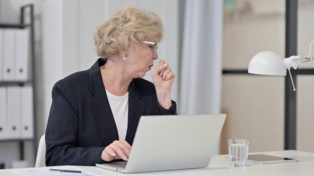 istock Old Businesswoman Coughing while Working on Laptop 1347087328