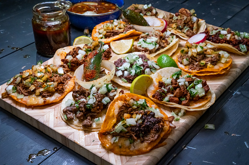 Delicious Variety Of Authentic Street Tacos Arranged On A Wood Platter With Lime Slices, Beef Consume And Chili Diarbo Sauce