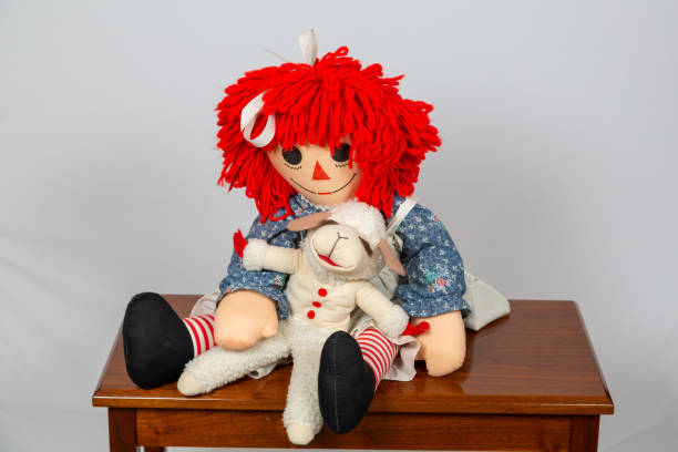 old rag doll with white apron & sheep spuppet itting on a wooden bench stock photo