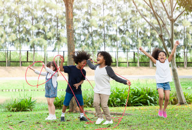 gruppo di bambini della diversità che giocano allegri nel parco. bambini che si divertono e saltano con la corda in giardino. - playground schoolyard playful playing foto e immagini stock