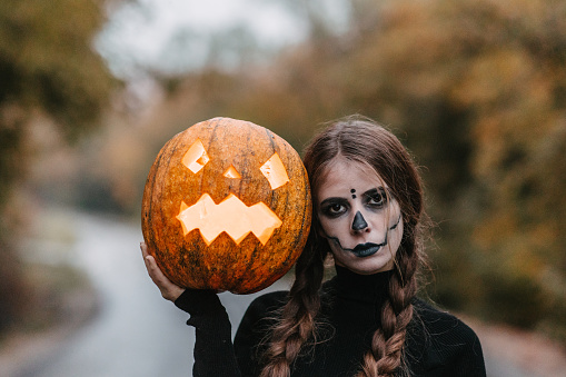 A young disguised woman leaning head on a carved Halloween pumpkin