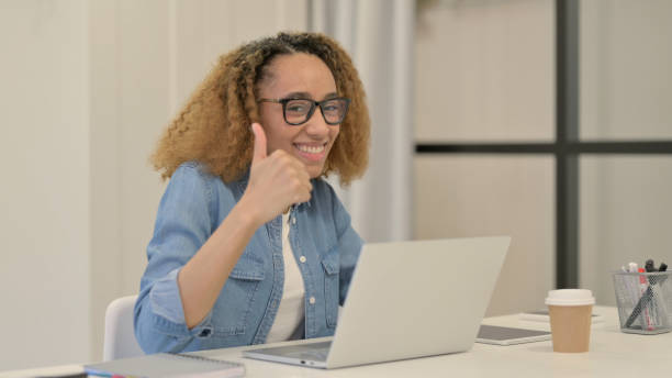 istock African Woman Showing Thumbs Up Sign While using Laptop in Office 1347091098