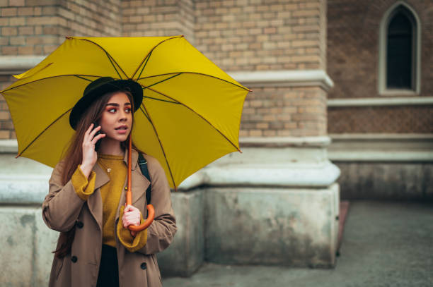 istock Young beautiful woman using a smartphone and holding a yellow umbrella 1347095793