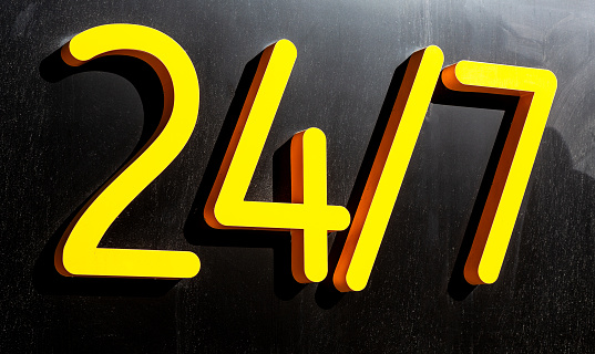 24 hours yellow sign open or working around the clock hanging on dark wall. Open sign. Day and night working. 24 hour concept