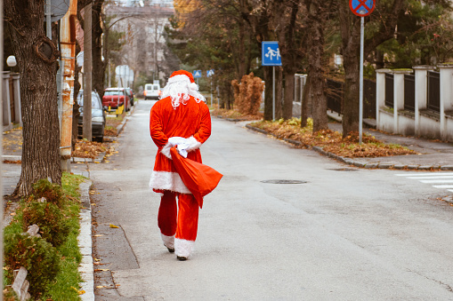 Santa Claus on his way to deliver presents walking on the street with a gift.