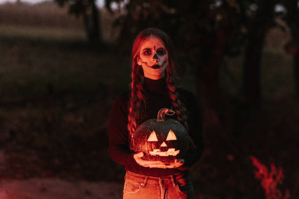 A young woman with stage make-up holding carved pumpkin for Halloween Portrait of a young woman with stage make-up illuminated by red stop lights holding carved Jack o’lantern pumpkin halloween pumpkin human face candlelight stock pictures, royalty-free photos & images