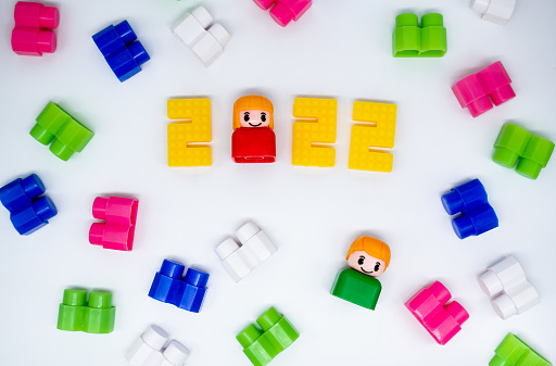 Colorful building blocks, toys plastic figures: girl in 2022 numbers and green boy on white background.