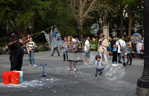 New York, New York, USA - June 1, 2019: African American man entertains people with large bubbles in Central Park.