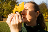 Young woman in profile with yellow leaves, sunlight, shadows, hands close up, autumn inspiration