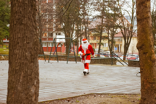 Santa Claus on his way to deliver presents walking in the city park with gifts.