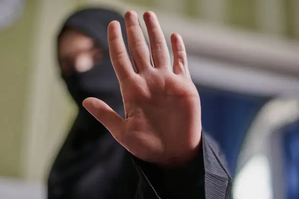 A Muslim woman in traditional black clothing nikab showing stop hand gesture. Role of women in Islamic world. Domestic violence, discrimination of Muslim women. Stop domestic violence against women