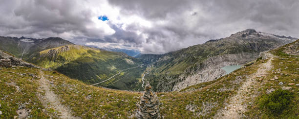 panoramic view from the Furka pass to the valley and the Grimsel pass in the swiss alps mountain landscape under dramatic cloudy skies with some sun rays on the mountains. the Furkapass is one of the most famous mountain pass roads. near the Hotel Belvedere and the Rhone Glacier, Canton Valais, Switzerland grimsel pass photos stock pictures, royalty-free photos & images