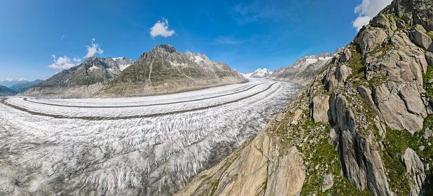 wide angle view of the glacier, its central moraines and the mountains on the side with a blue sky and a few clouds. the Aletsch Glacier is the largest glacier in the Alps. near Eggishorn, Fiescheralp and Bettmerhorn, canton of Valais, Switzerland