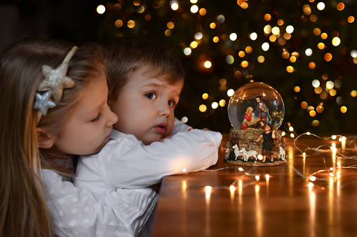 Brother and sister looking at a glass ball with a scene of the birth of Jesus Christ near christmas tree