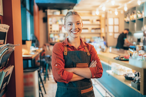 Portrait of young woman, bartender. Coffee shop working in apron smiling at camera
