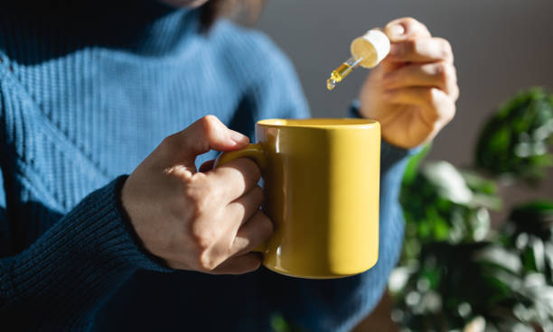 cbd hemp oil - woman taking cannabis oil in tea cup - focus on left hand - druppelfles stockfoto's en -beelden