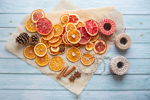cinnamon, anise, dried oranges and grapefruit slices, threads for diy projects, gift wrapping and beautiful eco Christmas decorations like wreaths arranged on a blue wooden table