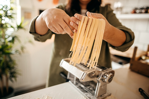 Photo of a young woman making homemade pasta in the kitchen of her apartment