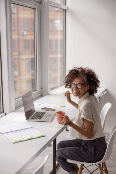 istock Smiling pretty woman holding coffee and pen while working 1347138464