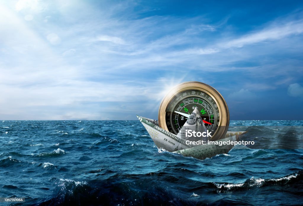 Business finance and industry concept of making money and prosperity Conceptual money boat carrying large compass in stormy seascape Direction Stock Photo