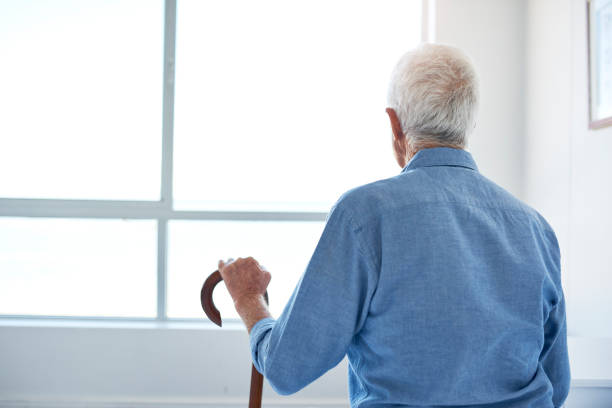 aufnahme eines älteren mannes, der auf dem bett sitzt und zu hause aus einem fenster schaut - senior adult depression dementia alzheimers disease stock-fotos und bilder