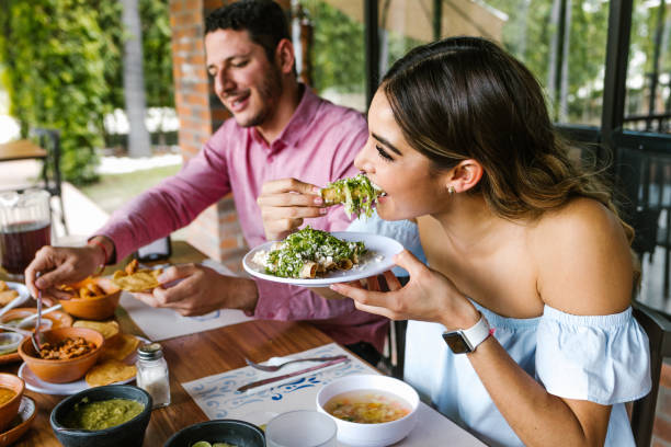 joven latina comiendo tacos mexicanos en la terraza de un restaurante en méxico latinoamérica, sintiéndose feliz en un día de verano - restaurante fotografías e imágenes de stock