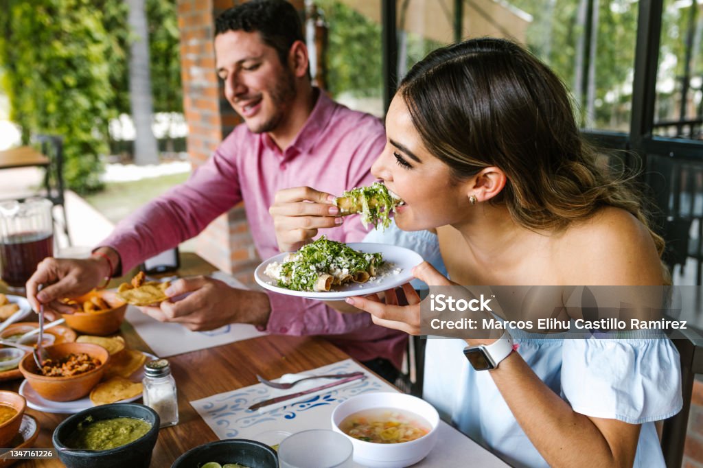 young latin woman eating mexican tacos on a restaurant terrace in Mexico Latin America, feeling happy on a summer day Eating Stock Photo