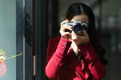 Young pretty female in a red suit with retro camera, taking picture, snap shot, focus the objects, hobby.