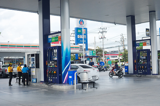 Daily scene at gas station in Bangkok Ladprao with gas attendants of PTT and some few customers. A car is at gas pump. In right area a person is with motorcycle at gas pump. In background is small super market Seven-Eleven