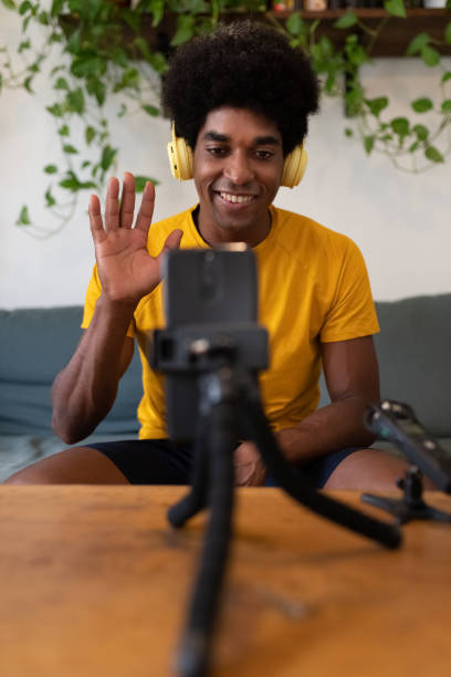 istock Young african american influencer waving hello to followers. Recording himself for tutorial on social media. Vertical 1347169813