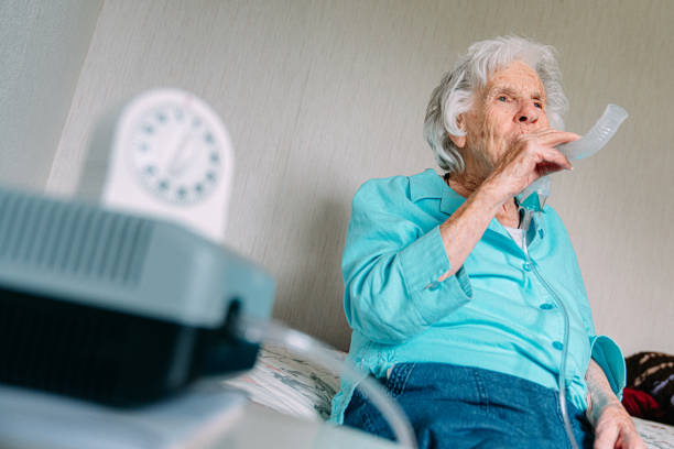 istock A Defocused Wind-Up Kitchen Timer Counts Down in the Foreground as a Senior Caucasian Woman Sits at Home Using a Nebulizer to Inhale Medication to Treat Asthma or Open Up Lung Airways 1347170778