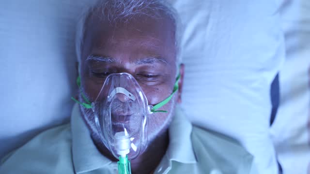 Close up Top view head shot of old breathing with ventilator oxygen mask at hospital due to coronavirus covid-19 breath shortness or dyspnea