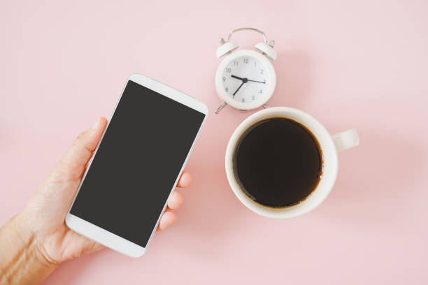istock senior's hand holding white mobile phone with clipping path on touchscreen with blurred analog alarm clock and a cup of hot coffee  on sweet pink background 1347175770