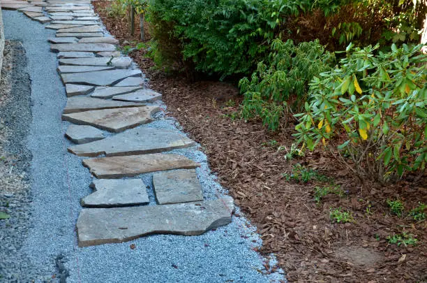 Photo of laying porphyry of large flat stones. the paving is laid in some gravel, the joints are then filled with pebbles. garden nature path made of brown irregular stone slabs