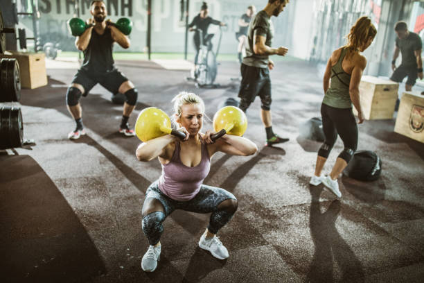 Large group of athletic people having gyms training in a gym. Large group of athletes exercising strength of cross training in a gym. Focus is on woman with kettle bells. circuit training stock pictures, royalty-free photos & images