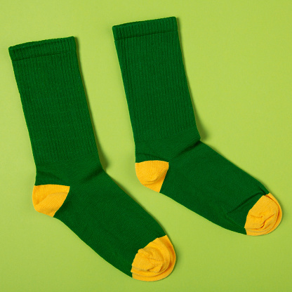 pair of stylish green socks with yellow heels and toes, on green background, lifestyle concept