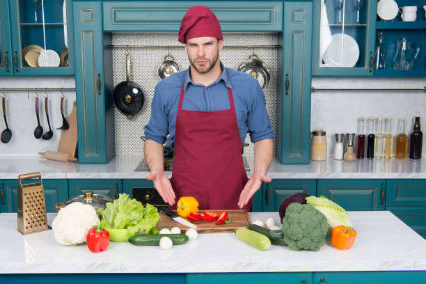 istock Man point at vegetables on table. Cook in chef hat and apron in kitchen. Ingredients for cooking dishes. Vegetarian menu and healthy diet. Food preparation and cooking recipes 1347185172